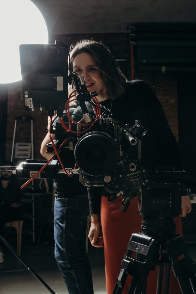 A female videographer adjusts studio camera equipment under soft lighting.